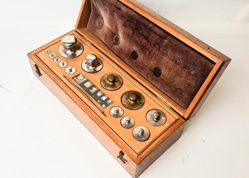 A wooden box with a set of 13 standard masses and one pair of tweezers. 